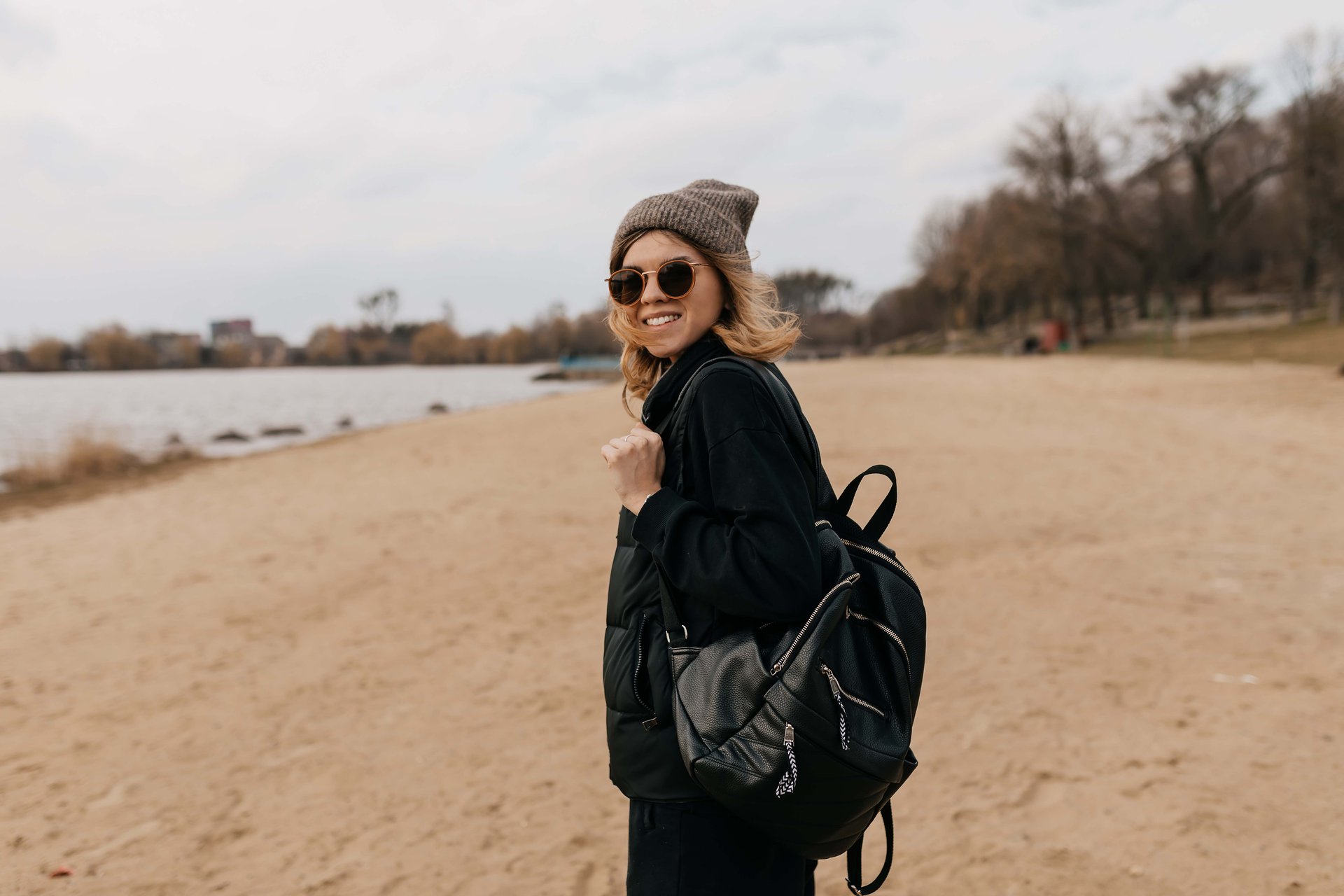 excited-lovely-pretty-girl-with-short-hairstyle-wearing-cap-with-backpack-in-sunglasses-is-walking-on-the-beach