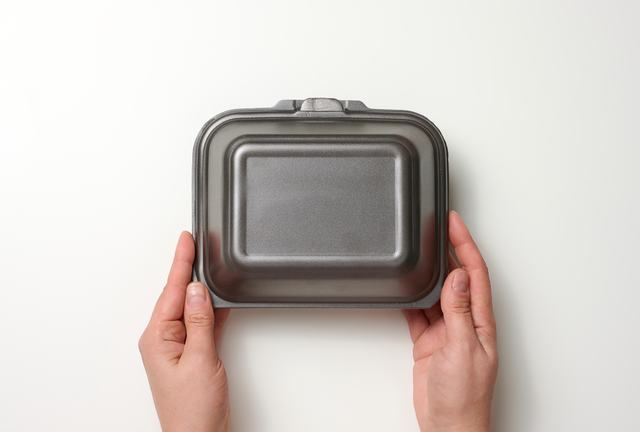 female-hand-holds-disposable-food-container-gray-box-of-polystyrene-on-white-background
