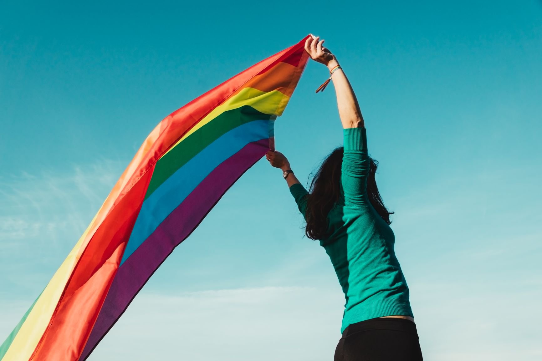 unrecognizable_young_girl_raising_gay_pride_flag_above_her_head.jpg