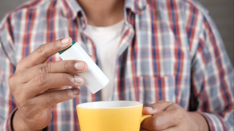 Young man putting artificial sweetener