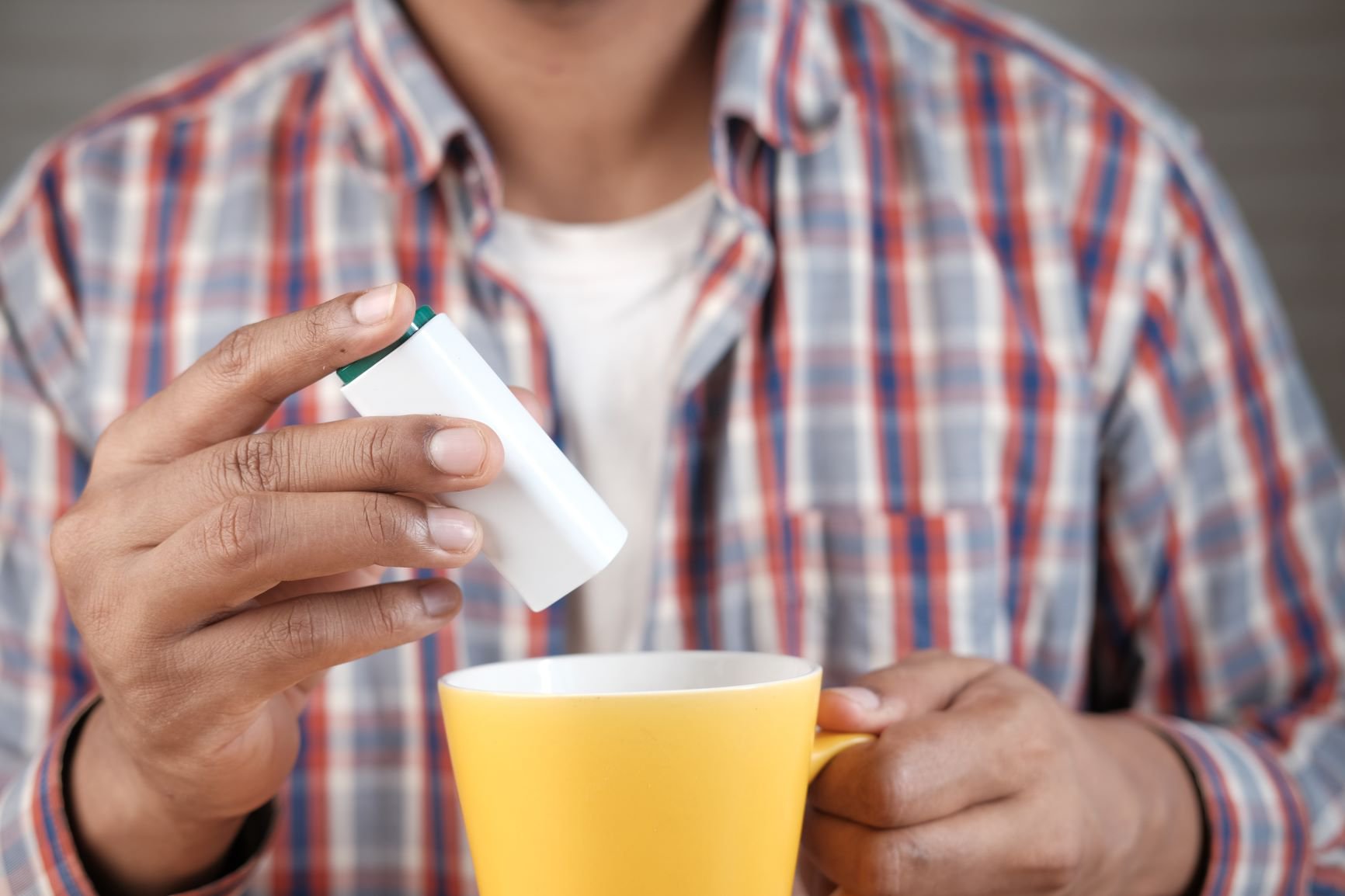 Young man putting artificial sweetener